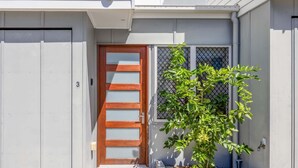 Uma casa com porta de madeira, uma pequena janela com mosquiteiro e um vaso com planta.
