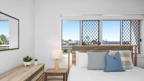Quarto com cama, mesa de cabeceira, abajur e janela com vista.
