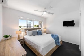 Ein Schlafzimmer mit Bett, Nachttischen, Deckenventilator, Fernseher und Fenster mit Blick.