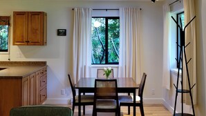A dining area with a table and chairs, a window with curtains, a wooden cabinet, and a black floor lamp.