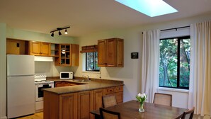 A kitchen with wooden cabinets, a central island, a dining table with chairs, and a window with curtains.