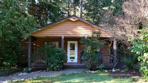 A small wooden cabin with a porch, surrounded by dense greenery.