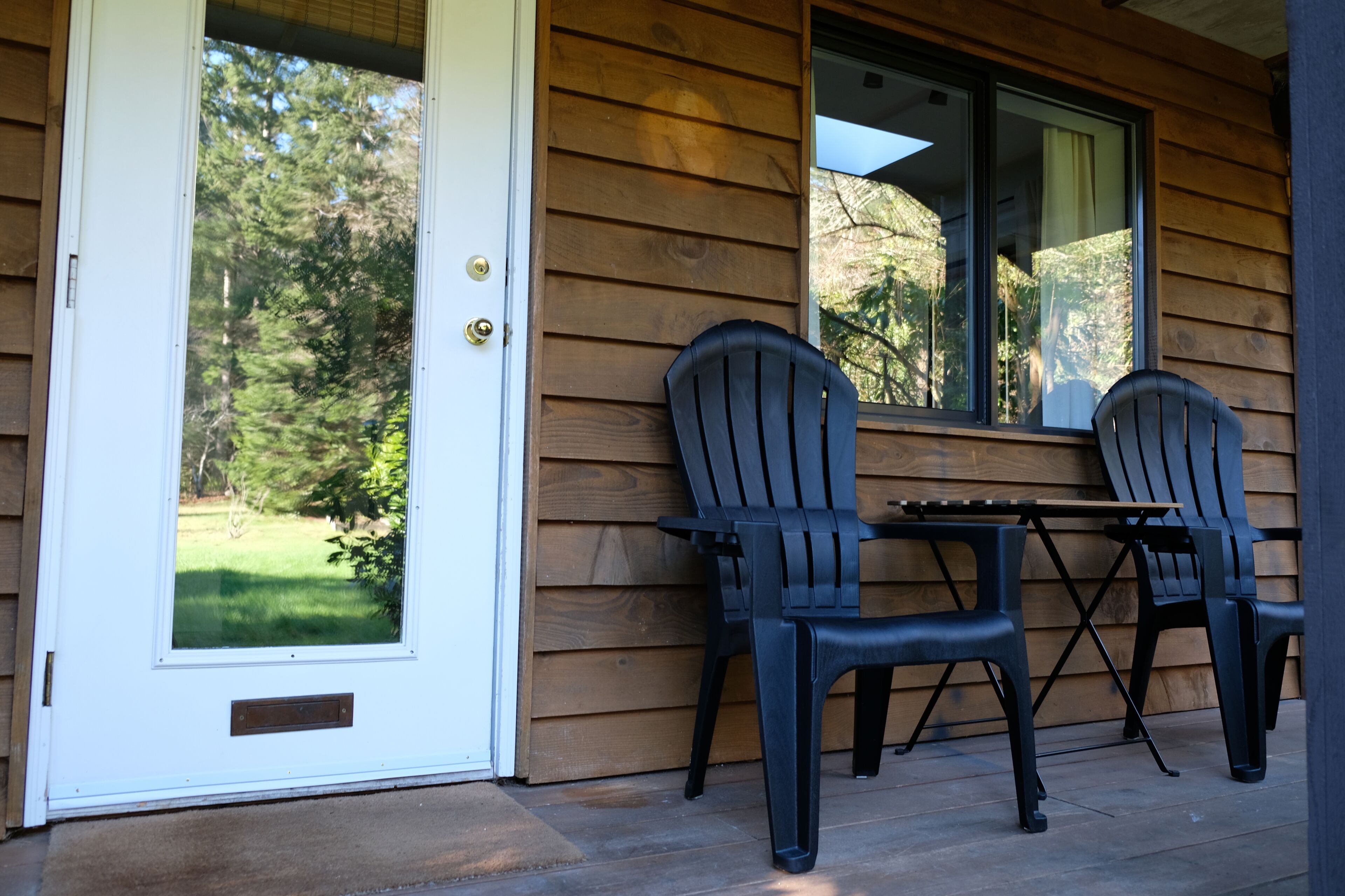 A wooden exterior with a white door, two black chairs, and a small table.