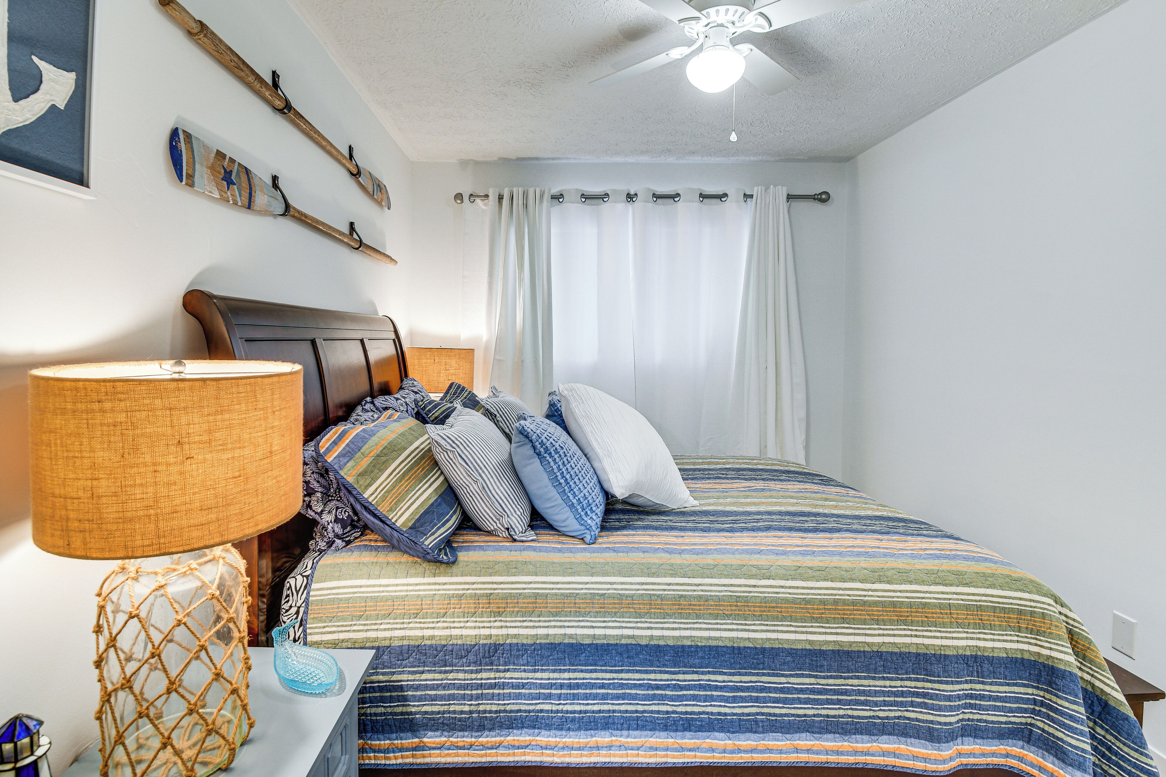 A bedroom with a bed, a lamp, a ceiling fan, and a window with curtains.