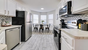 A modern kitchen with white cabinets, stainless steel appliances, a dining area with a table and chairs, and a brick-patterned backsplash. - < 1 Mi to Historic McKinney: Modern Duplex w/ Yard (McKinney)
