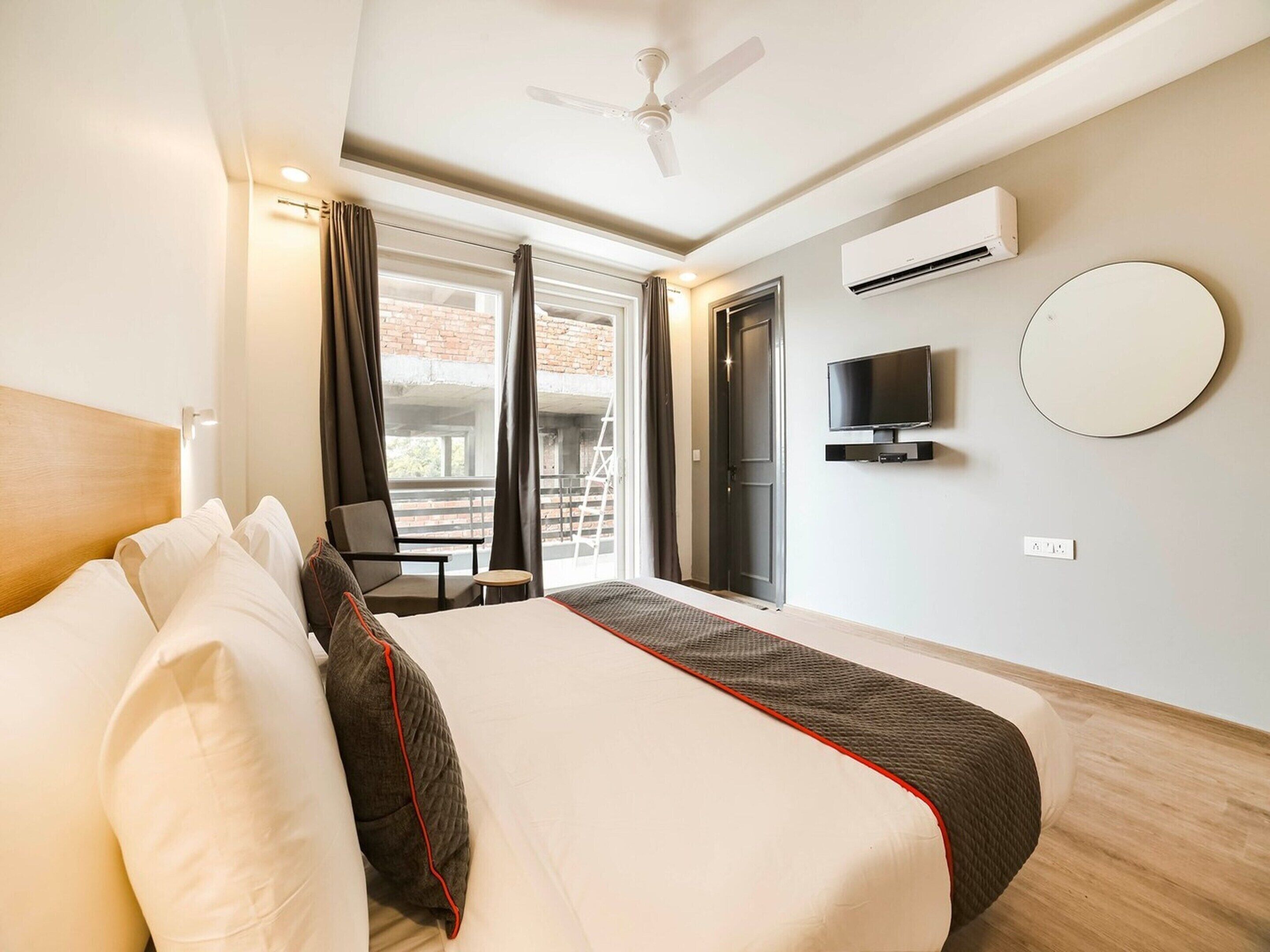 Habitación de hotel con cama, televisión, aire acondicionado, balcón con una silla y vistas al exterior.