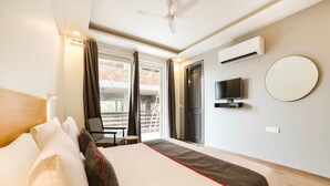 A hotel room with a bed, a TV, an air conditioning unit, a balcony with a chair, and a view of the outside. - Townhouse Sector 46 Gurgaon Near Appu Ghar (Gurugram)