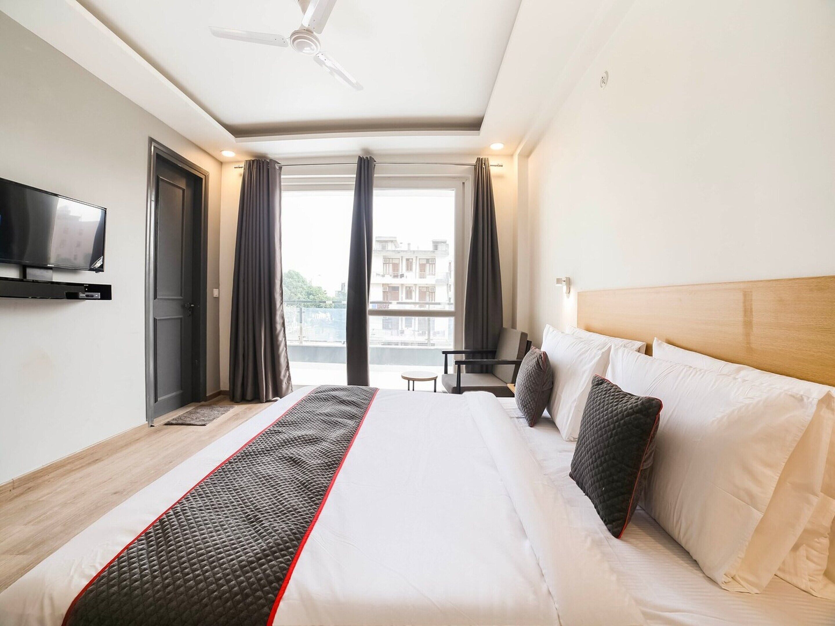 Ein Hotelzimmer mit Bett, Wandfernseher, Schreibtisch und Blick auf die Stadt durch große Fenster.