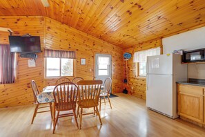 A wooden cabin interior with a dining table, chairs, a television, a refrigerator, and a microwave. - Fish, Float & Ride the Trails! Northwoods Retreat (Pearson)