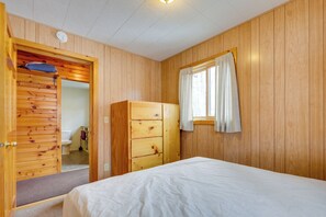 A wooden-paneled room with a bed, a wardrobe, and a bathroom visible through an open door. - Fish, Float & Ride the Trails! Northwoods Retreat (Pearson)
