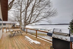 A wooden deck with a grill and picnic table, overlooking a body of water and a dock. - Fish, Float & Ride the Trails! Northwoods Retreat (Pearson)