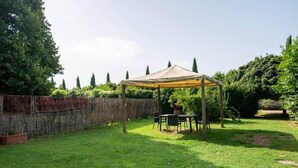 Un patio couvert, agrémenté d’une table et de chaises, entouré d’une clôture en bois et de verdure.