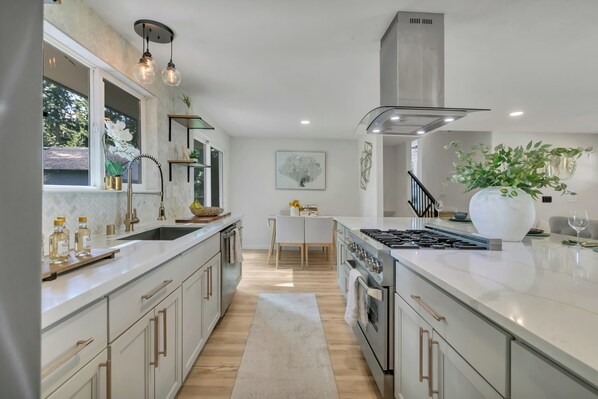 Une cuisine moderne dotée d’un îlot central, d’appareils électroménagers en acier inoxydable et de luminaires suspendus.