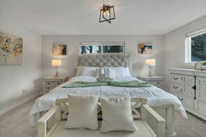 Une chambre à coucher avec une tête de lit capitonnée, deux tables de chevet avec des lampes, une fenêtre donnant sur un beau paysage et une commode avec des tiroirs.