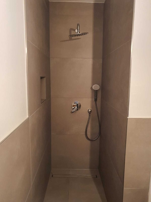 Ein kleiner, abgeschlossener Duschbereich mit Handbrause und Wandarmatur.