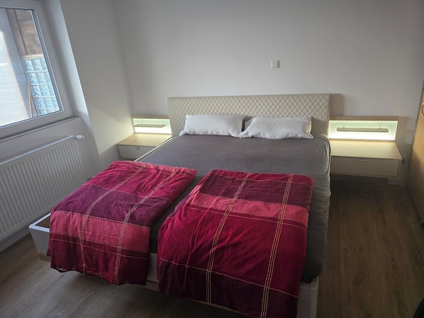 Een slaapkamer met een bed, twee nachtkastjes, een raam en een radiator.