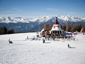 A snow-covered ski slope with a large gathering around a tipi-like structure, ski lifts in the background, and mountains in the distance. - Cosy Apartment in a Central Location (Veysonnaz)