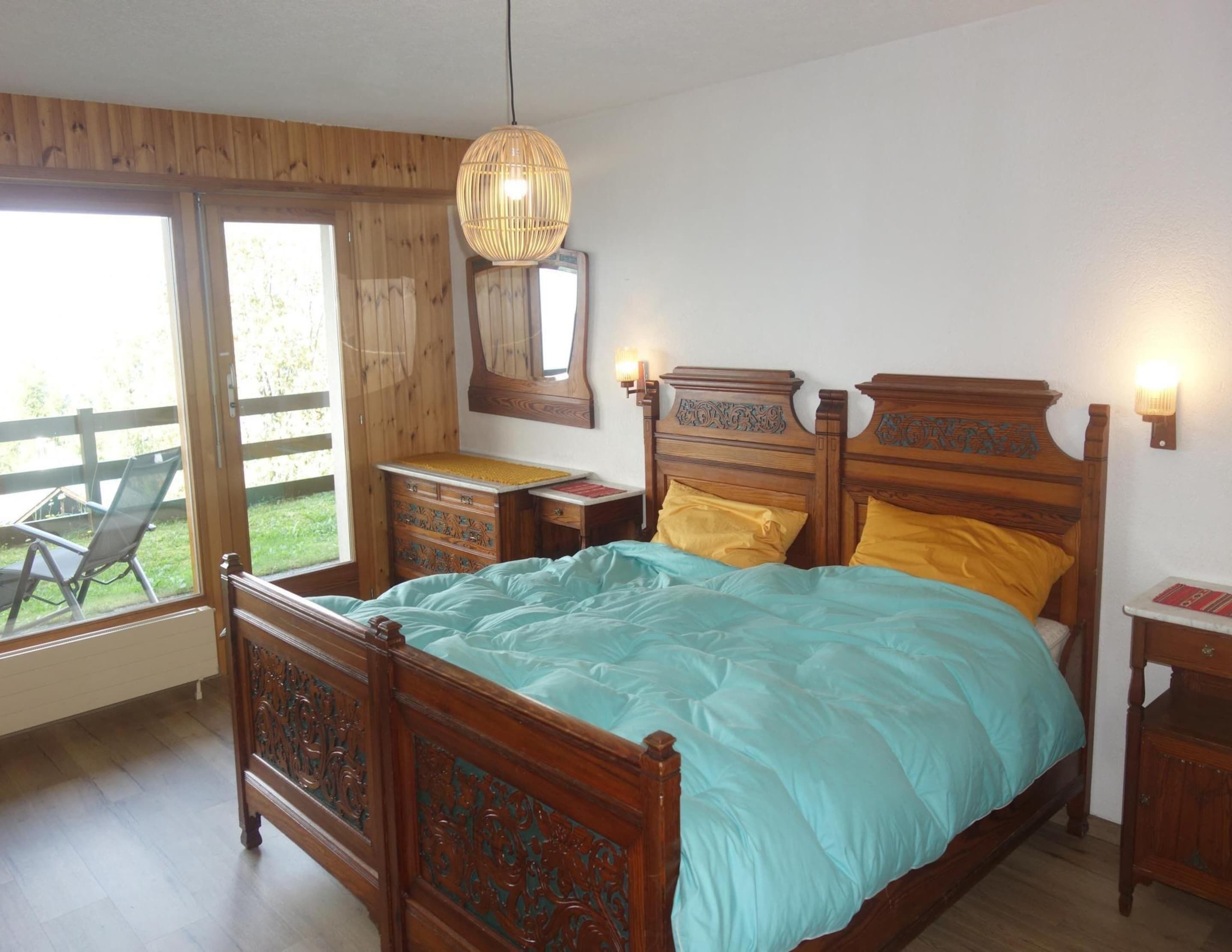 A bedroom with a wooden bed, a dresser, a mirror, and a hanging light fixture.