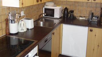 A compact kitchen with a stove, microwave, toaster, sink, and a small refrigerator.