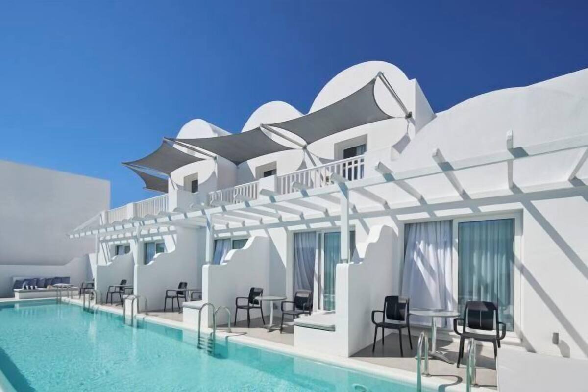 Ein Poolbereich mit Liegestühlen und Sonnenschirmen, umgeben von weißen Gebäuden mit Balkonen.