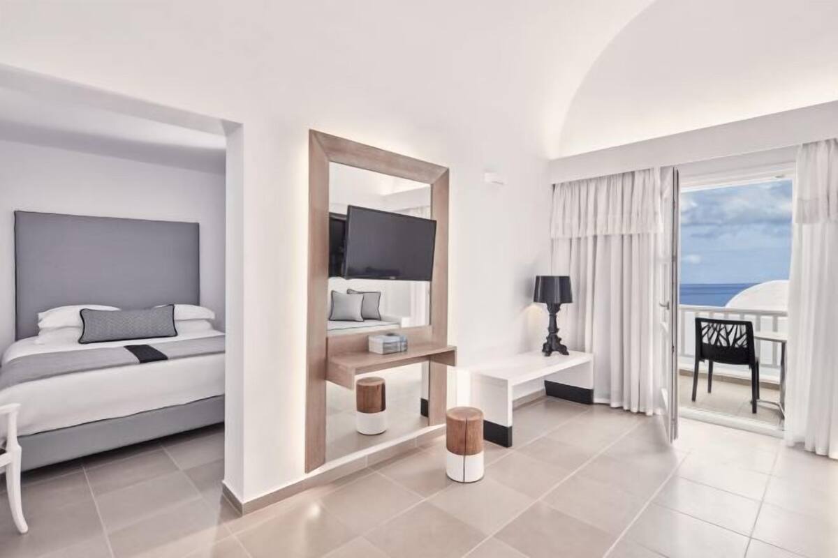 Ein modernes Hotelzimmer mit Bett, Fernseher, Schreibtisch und Balkon mit Blick.