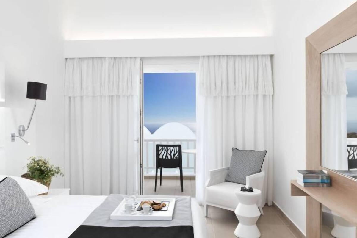 Ein Hotelzimmer mit Bett, einem kleinen Tisch mit einer Speisewagenplatte, einem Sessel, einer Couch und einem Balkon mit Blick.