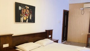 A hotel room with a large bed, a wooden headboard, a nightstand, a bedside table, and a painting on the wall. - Hotel Sandriana Kandy (Kandy)