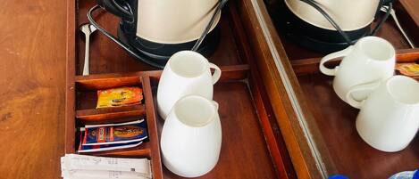 Una bandeja de madera con una cafetera, tazas blancas, una cuchara, aperitivos y botellas de agua.