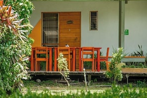 Un bâtiment doté d’une porte en bois, d’une fenêtre et d’un petit espace extérieur aménagé avec des chaises.