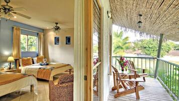 A bedroom with two beds, a ceiling fan, and a balcony with wooden chairs and a table.