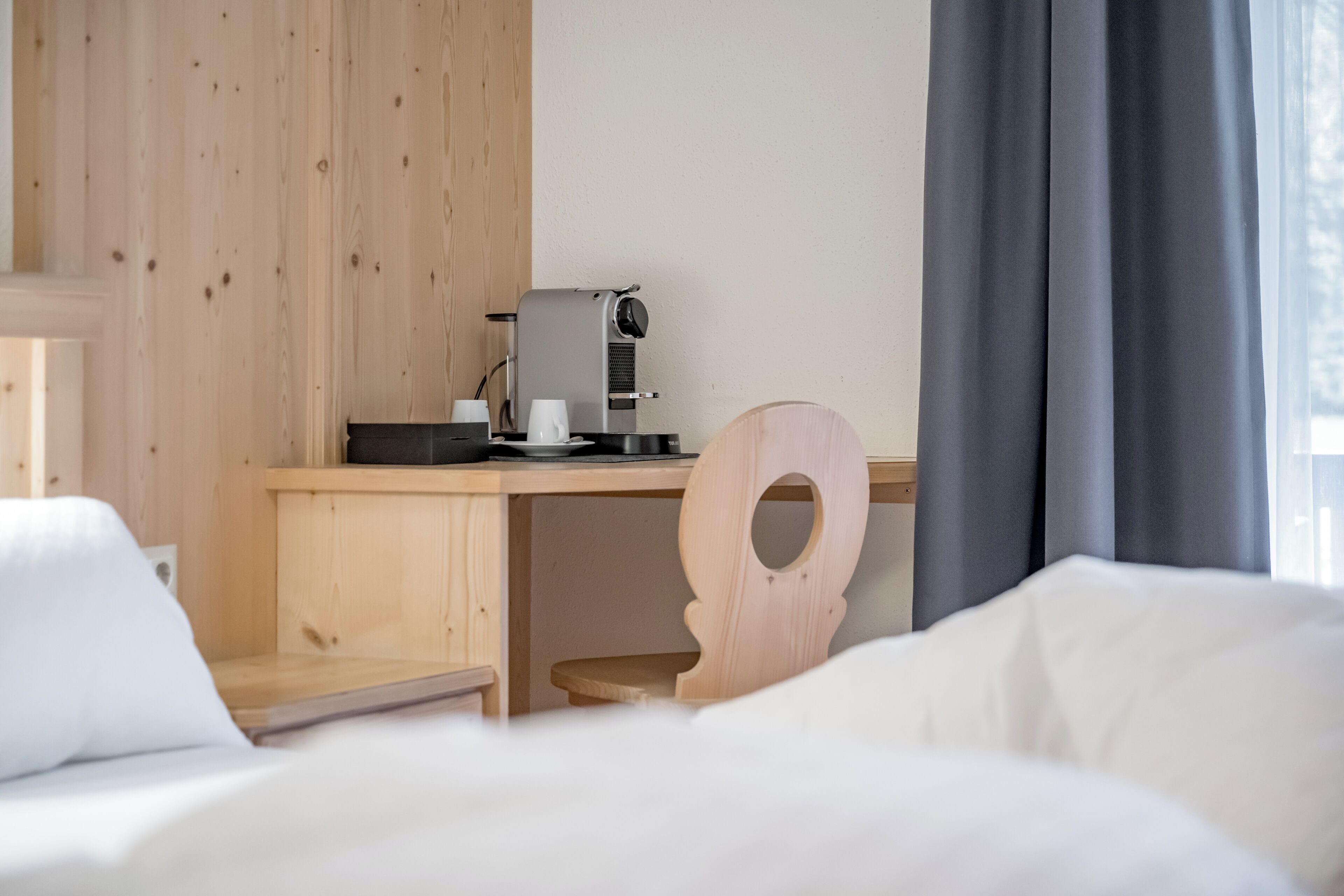 Une chambre d’hôtel avec un bureau en bois, une machine à café, une chaise en bois et un lit avec une literie blanche.