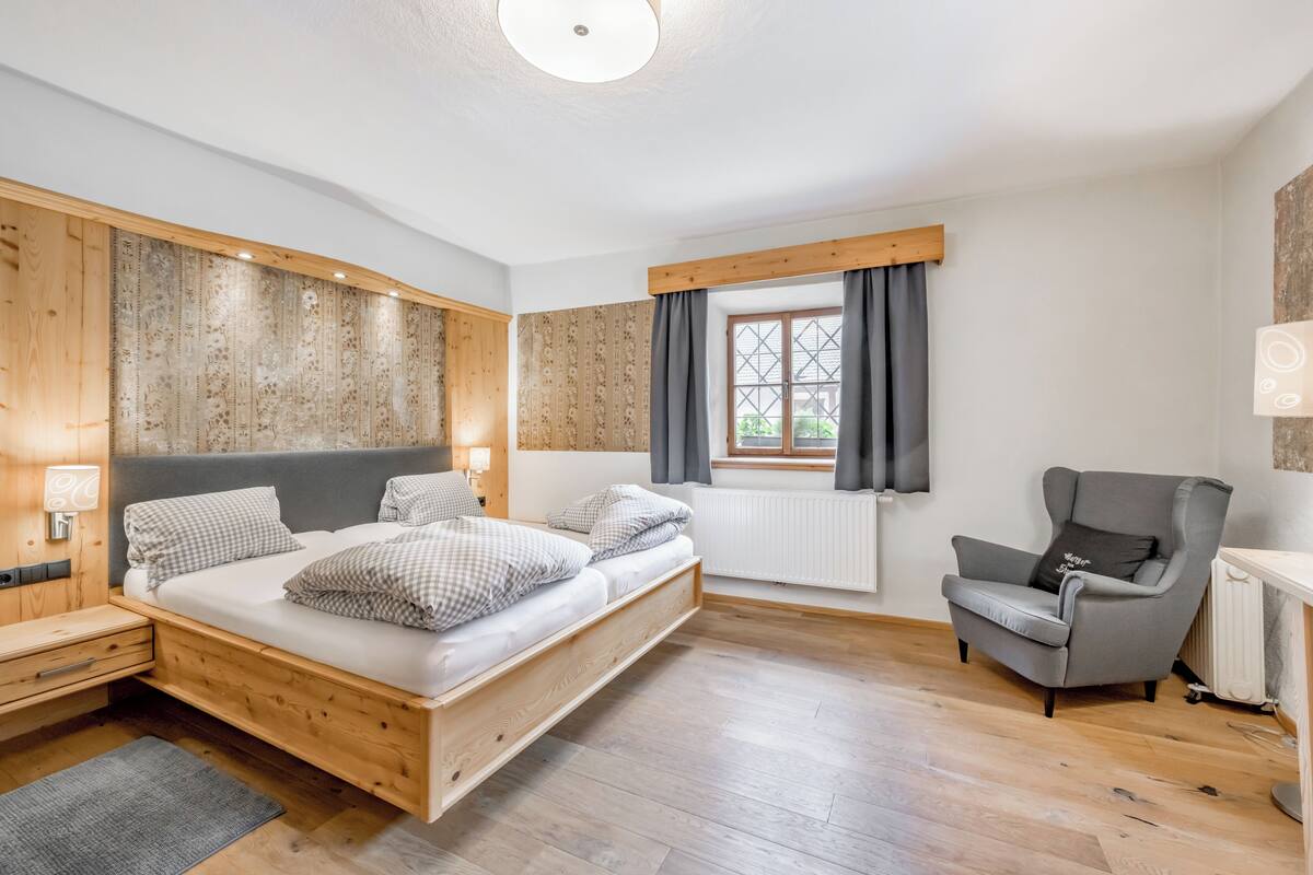 Un dormitorio con cama de madera, una silla, una ventana con cortinas y un radiador.