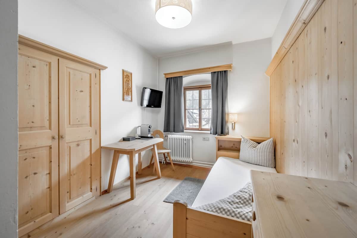 Una habitación con cama, escritorio, silla, televisor y ventana con cortinas.
