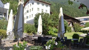 An outdoor patio with tables and chairs, umbrellas, and a building in the background. - Gasthof Stern (Oetz)