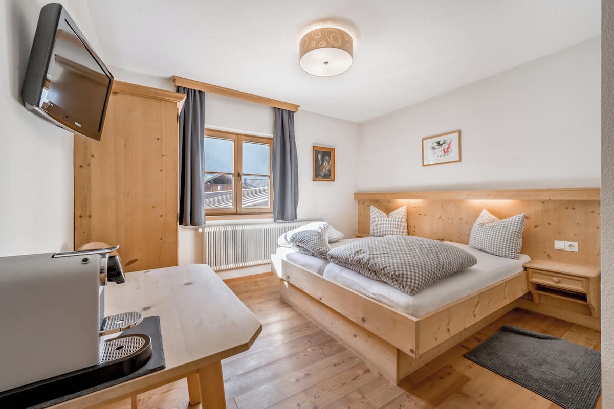 Un dormitorio con cama, escritorio, televisor, ventana con cortinas e iluminación en el techo.