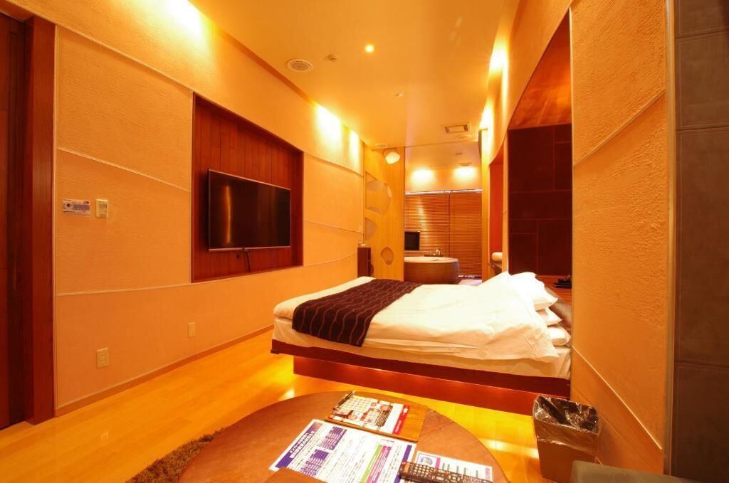 A modern hotel room with a bed, a television, a small table with a menu, and a trash bin.