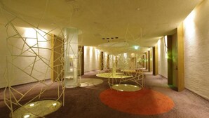 Ein Hotelkorridor mit geometrischen Leuchten, runden Plattformen und einem Teppichboden.