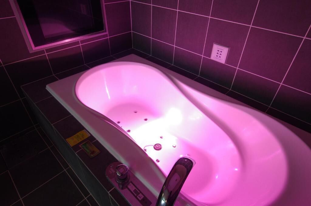 A modern bathroom with a white bathtub, pink lighting, and a control panel.