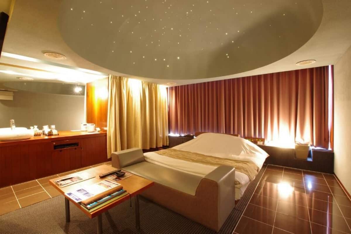 Une chambre d’hôtel comprenant un lit, un bureau, une chaise, une coiffeuse avec un miroir et des rideaux.