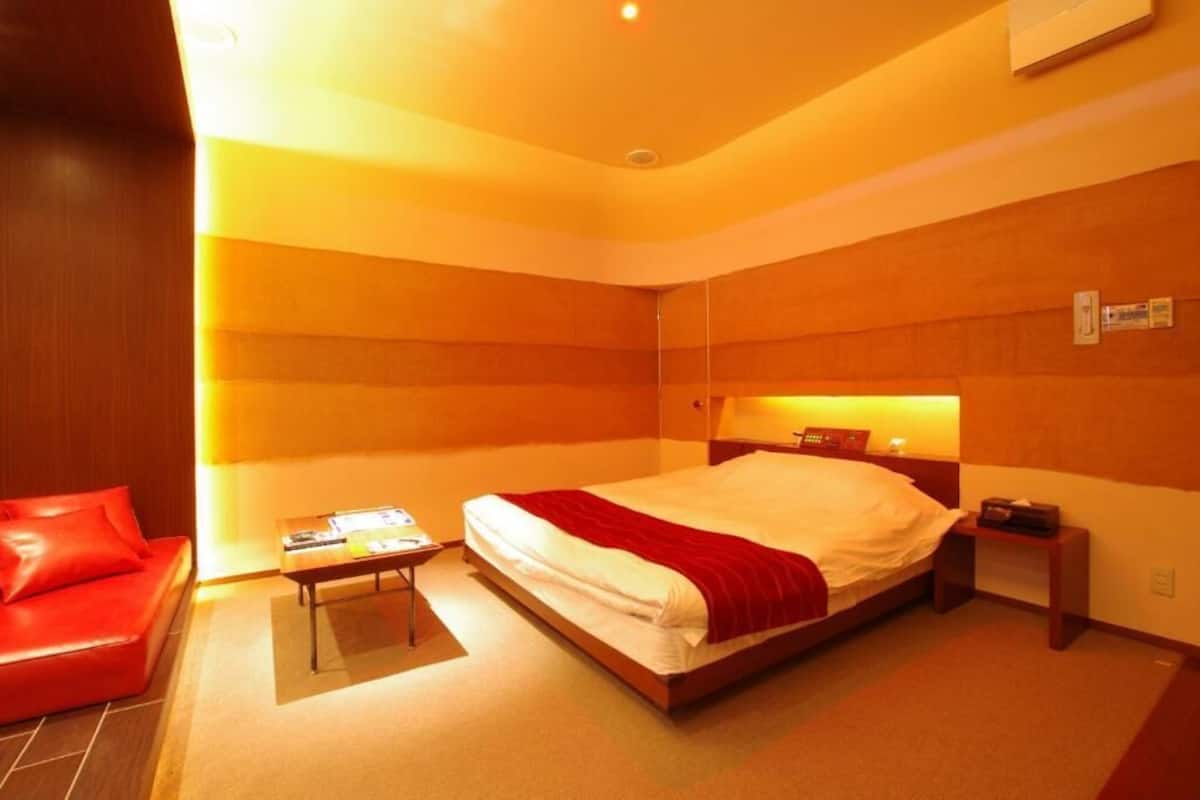 Une chambre d’hôtel avec un lit, un canapé rouge, une petite table et une table de chevet.