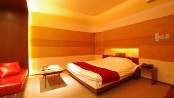 Quarto de hotel com uma cama, um sofá vermelho, uma mesinha e uma criadeira.