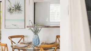 A dining area with a glass table, wooden chairs, a hanging light fixture, and wall art. - A Noosa Gem on Noosa Parade - close to everything (Noosa Heads)