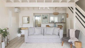 A living room with a grey sofa, a wooden chair, a white rug, and a staircase. - A Noosa Gem on Noosa Parade - close to everything (Noosa Heads)