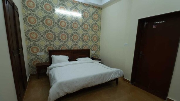 Quarto com cama, mesa de cabeceira, papel de parede estampado, porta e chão em azulejo.