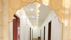 Um corredor com arcos ornamentados, piso de mármore e portas em ambos os lados.