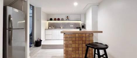 A modern kitchen with a central island, a stainless steel refrigerator, and a black stool.
