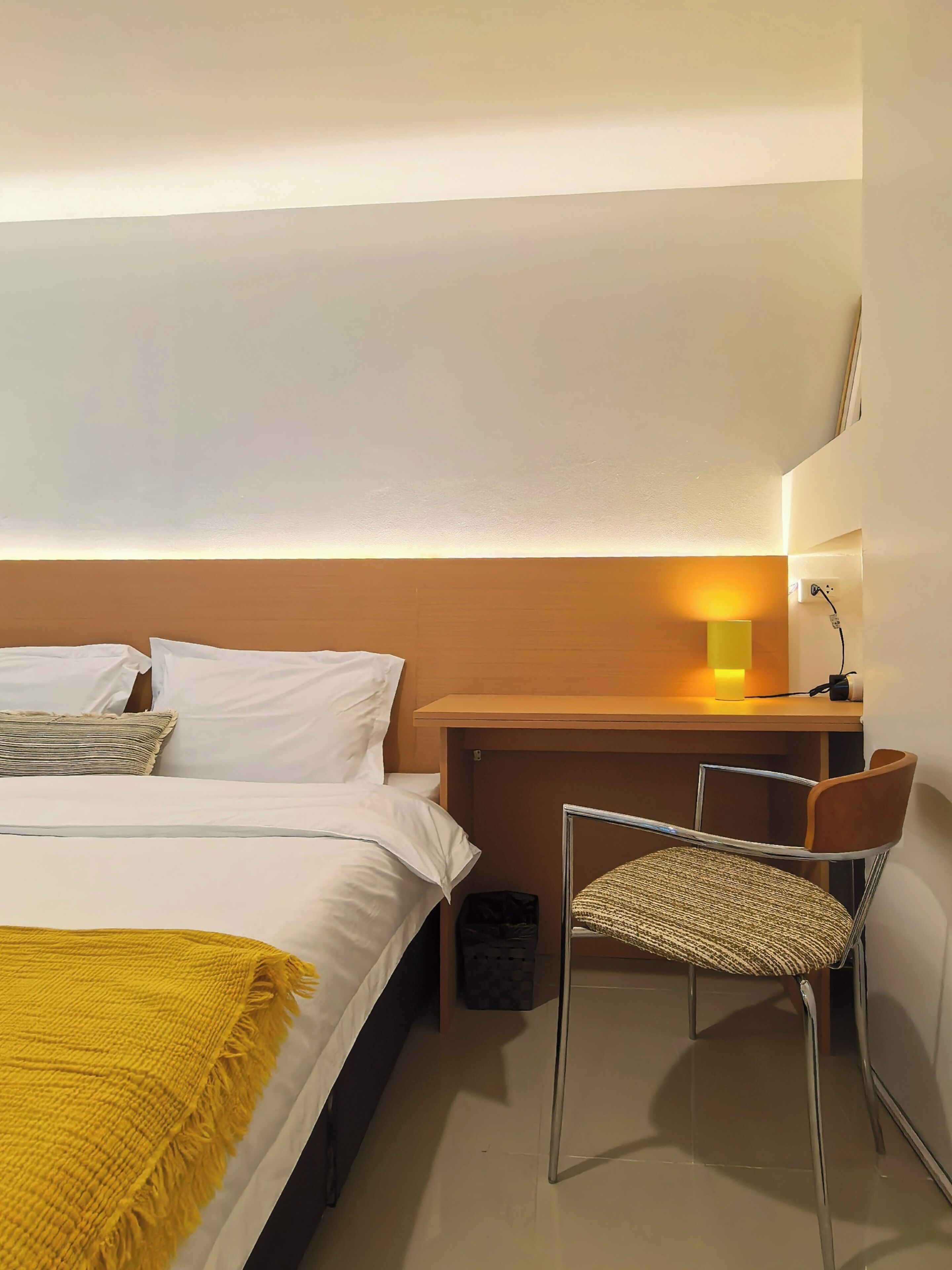 Une chambre d’hôtel équipée d’un lit, d’un bureau, d’une chaise, d’une lampe et d’une poubelle.