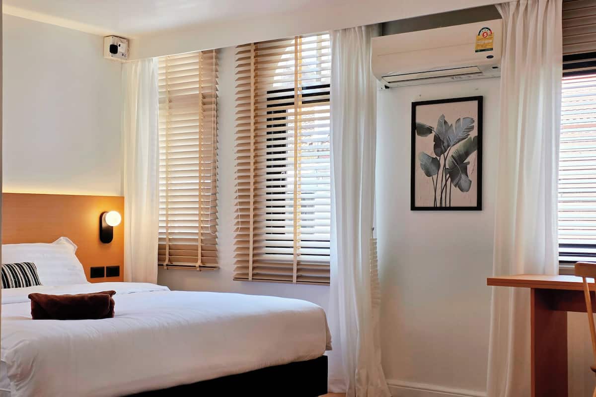 A hotel room with a bed, a desk, a wall-mounted air conditioner, and a framed picture.