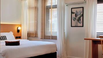 A hotel room with a bed, a desk, a wall-mounted air conditioner, and a framed picture.