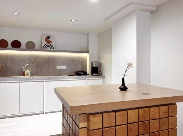 A modern kitchen with a wooden island, white cabinets, and a coffee machine.